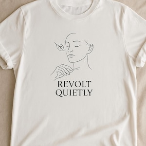 Könnte beinhalten: Weißes T-Shirt mit einer minimalistischen Strichzeichnung einer Person, die ein Blatt hält, und den Worten "REVOLT QUIETLY" in Schwarz. Das Design ist auf der Vorderseite des T-Shirts zentriert, das kurze Ärmel und einen Rundhalsausschnitt hat.