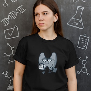 May include: Black t-shirt featuring a cartoon thyroid gland with a tired expression, holding a coffee mug that says "TSH". The word "TIRED" is written in white chalk on the chalkboard background, along with science-related doodles.