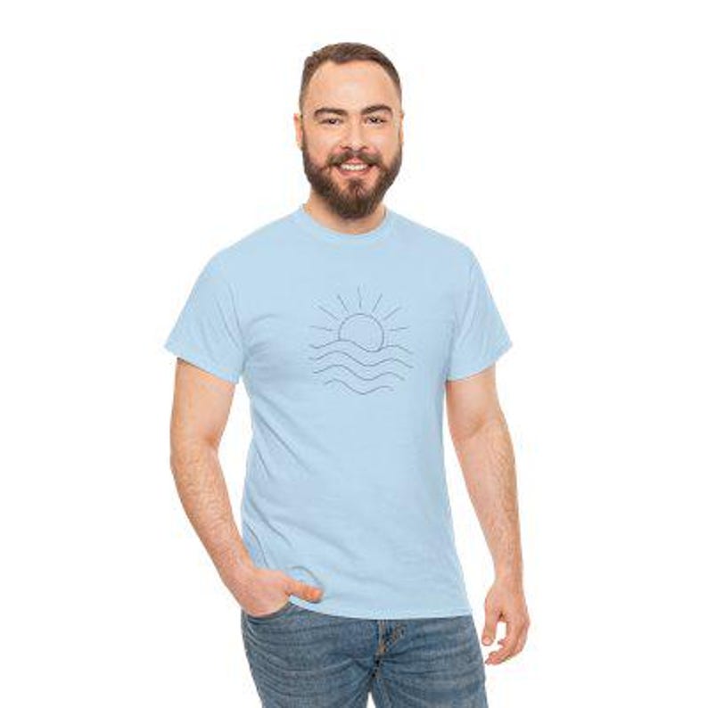 Puede incluir: Camiseta azul claro con un dise&ntilde;o minimalista de un sol sobre olas del mar en negro. La camiseta est&aacute; hecha de un material suave y es adecuada para ropa casual.