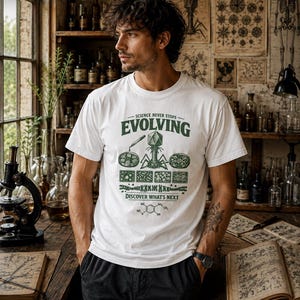 Può includere: Una t-shirt bianca a maniche corte con una stampa grafica verde scuro che riporta il testo "SCIENCE NEVER STOPS EVOLVING" e "DISCOVER WHAT'S NEXT". Il design include un batteriofago, piastre di Petri, cellule microscopiche e una formula chimica.
