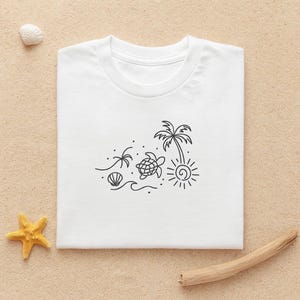 Può includere: T-shirt bianco con un disegno a tratto nero di una scena sulla spiaggia. Il design include una palma, un sole, una tartaruga, una conchiglia e delle onde. La maglietta è esposta su una superficie sabbiosa con una stella marina, una conchiglia e del legno alla deriva.