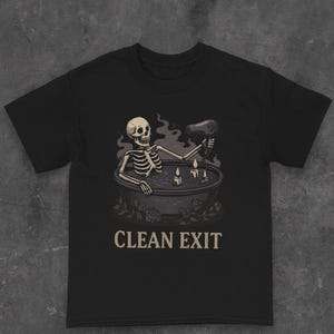 Può includere: T-shirt nero con una grafica umoristica di uno scheletro in una vasca da bagno con un asciugacapelli. Il design include candele e la scritta "CLEAN EXIT". Il tema è gotico e umoristico.