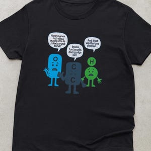 May include: Black t-shirt featuring cartoon-like illustrations of chemical elements with speech bubbles. The text in the bubbles reads, "Haroyouever iročeâtsa malkw ittle is poli-kisar yue bund?" and "Imake fout anadk dom gudge line!" and "And Ifust wanted one dectron..."