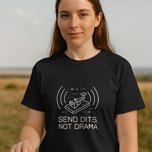 Könnte beinhalten: Schwarzes T-Shirt mit einer weißen Grafik einer Morsetaste und dem Text "SEND DITS, NOT DRAMA". Das T-Shirt wird von einer Person getragen. Eine Morsetaste befindet sich auf einer Holzoberfläche.