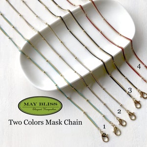 May include: A set of ten gold mask chains with different colored accents. The chains are displayed on a white plate and numbered 1 through 4. The text "MAY BLISS Elegant Keepsakes" and "Two Colors Mask Chain" is visible below the chains.