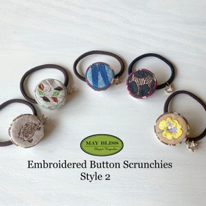 Könnte beinhalten: Fünf bestickte Knopf-Haargummis mit verschiedenen Designs. Die Designs beinhalten eine Jeans, ein Zebra, ein Igel, Herbstblätter und eine gelbe Blume. Die Haargummis sind aus braunem und schwarzem Gummiband mit einem goldenen Anhänger.
