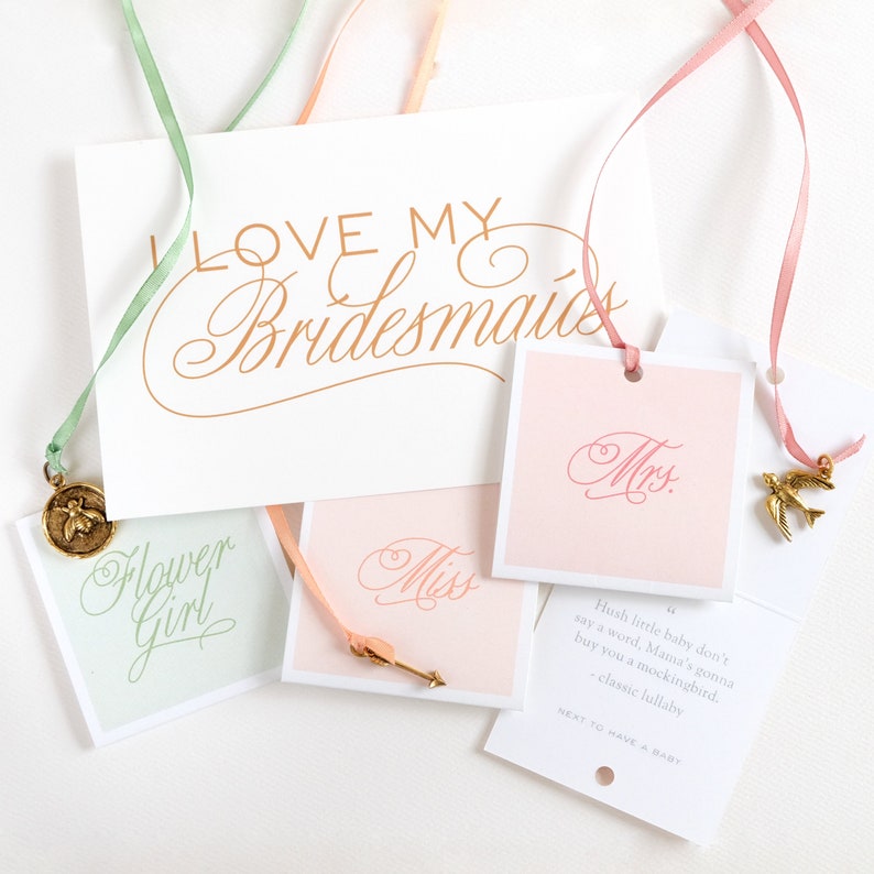 May include: A set of four gift tags with pink, peach, and green ribbons. The tags feature calligraphy text that says "Miss", "Mrs", "Flower Girl", and "Hush little baby don't say a word, Mama's gonna buy you a mockingbird. -classic lullaby NEXT TO HAVE A BABY".