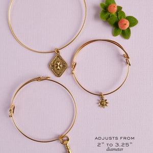 May include: Three gold adjustable bangles with charms. The bangles adjust from 2 to 3.25 inches in diameter and 7 to 10 inches in circumference. The charms are a key, a flower, and a decorative design.  "ADJUSTS FROM 2" TO 3.25" diameter 7" TO 10" circumference WILL FIT FLOWER GIRLS NO TOOL REQUIRED TO ADD CHARM"