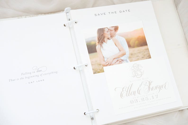 Pode incluir: &Aacute;lbum de casamento branco aberto com uma foto de um casal. O &aacute;lbum inclui um cart&atilde;o "Save the Date" com nomes e uma data, e uma cita&ccedil;&atilde;o: "Falling in love. That is the beginning of everything."