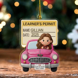 May include: A pink car-shaped ornament with a learner's permit design. The permit reads "LEARNER'S PERMIT, NAME: GILLIAN, DATE: 2025." A cartoon girl is driving the car. The license plate says "CA Look out world, here I come!"