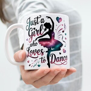 May include: White ceramic mug featuring a ballerina silhouette with a galaxy-themed tutu. The mug has the text "Just a Girl who Loves to Dance" in a script font, with hearts and musical notes.
