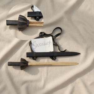 May include: A wooden sword with a black handle and a black sheath. The handle has a decorative, textured design. The text "Swordrep" is written on a white paper tag. The sword is displayed on a neutral-colored surface.
