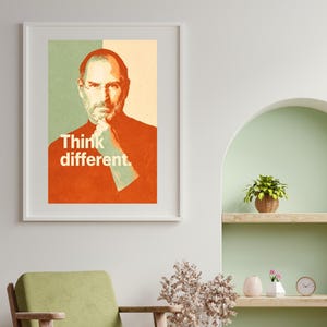 Könnte beinhalten: Gerahmter Kunstdruck mit dem Text "Think different" und einem Porträt eines Mannes. Das Kunstwerk verwendet einen Retro-Stil mit Orange-, Grün- und Beigetönen. Der Druck befindet sich in einem weißen Rahmen und verleiht dem Raum eine stilvolle Note.