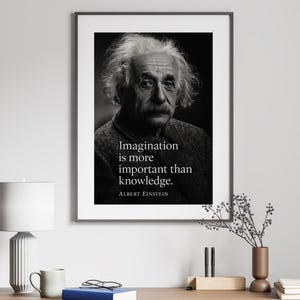 Può includere: Una stampa in bianco e nero incorniciata con un ritratto di Albert Einstein e la citazione "L'immaginazione è più importante della conoscenza". La stampa è esposta su una scrivania di legno con una lampada, una tazza e dei libri.