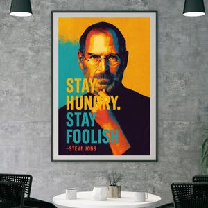 Puede incluir: Un póster motivacional con un retrato de Steve Jobs en estilo pop art. El póster tiene un fondo amarillo, azul y naranja con la cita "Stay Hungry. Stay Foolish." - Steve Jobs.