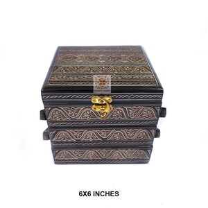 May include: A black wooden box with ornate silver-coloured carvings and a gold-coloured clasp. The box measures 15 x 15 cm. The text "6X6 INCHES" is at the bottom of the image.