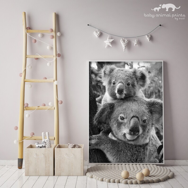 May include: Black and white photograph of a mother koala and her joey. The mother koala is sitting on a tree branch and the joey is sitting on her back. The photograph is framed in a white frame.