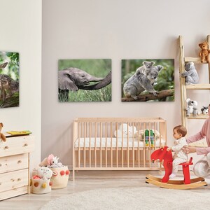May include: A nursery room with a wooden crib, a wooden dresser, and a wooden rocking horse. There are three framed animal prints on the wall, a deer, an elephant, and a koala. A woman is sitting on the floor with a baby on the rocking horse.