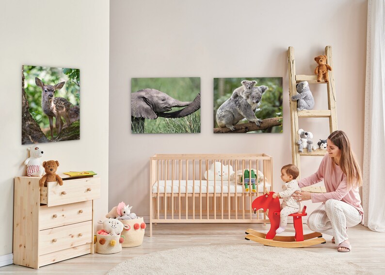 May include: A nursery room with a wooden crib, a wooden dresser, and a wooden rocking horse. There are three framed animal prints on the wall, a deer, an elephant, and a koala. A woman is sitting on the floor with a baby on the rocking horse.