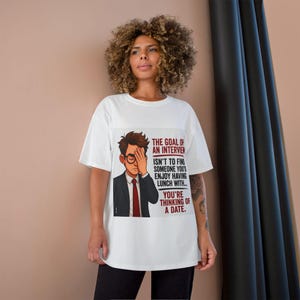 May include: A white short-sleeved t-shirt featuring a graphic of a person in a suit and glasses with their hand over their face. The text reads: The goal of an interview isn't to find someone you'd enjoy having lunch with... you're thinking of a date.