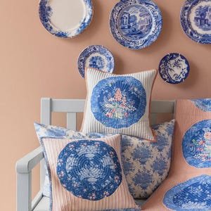 Peut inclure: Présentation de plaques décoratives bleues et blanches sur un mur pêche, avec des coussins et une courtepointe assortis sur un banc bleu clair. Les coussins et la courtepointe présentent des motifs floraux et circulaires.
