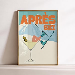 Op de afbeelding: Een ingelijste wandkunstprint met een martiniglas gevuld met een gele vloeistof en twee groene olijven. In het glas bevinden zich benen met turkooiskleurige skischoenen en ski's. De achtergrond toont besneeuwde bergen met de oranje tekst APRÈS SKI.