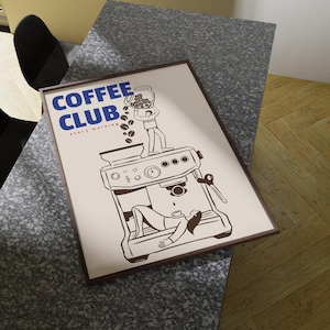 May include: A framed rectangular poster with a cream background featuring a black line drawing of an espresso machine. The text COFFEE CLUB is printed in blue, with every morning in red. A figure pours coffee beans into the machine top.