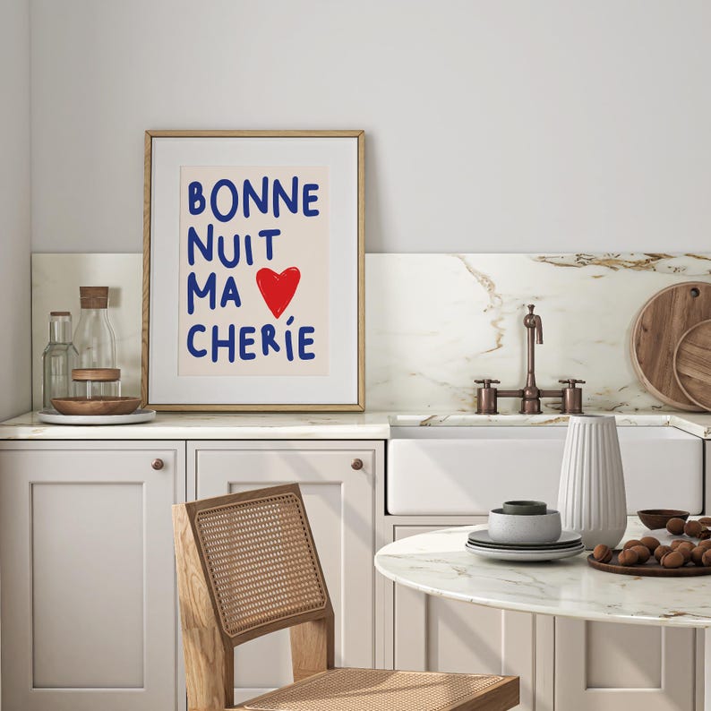 May include: A framed print with the text "BONNE NUIT MA CHERIE" in blue lettering with a red heart in the middle of the text. The print is hanging on a white wall above a kitchen sink.
