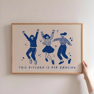 Peut inclure: Une affiche encadrée avec une illustration bleue de trois personnages dansant. Les personnages portent différentes tenues, les bras levés. Le texte "THIS KITCHEN IS FOR DANCING" est imprimé en bleu en bas de l'affiche.