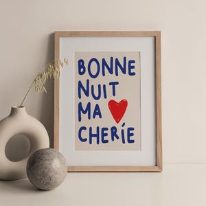 May include: A framed print with the text "BONNE NUIT MA CHERIE" in blue lettering and a red heart. The background is a light beige color.