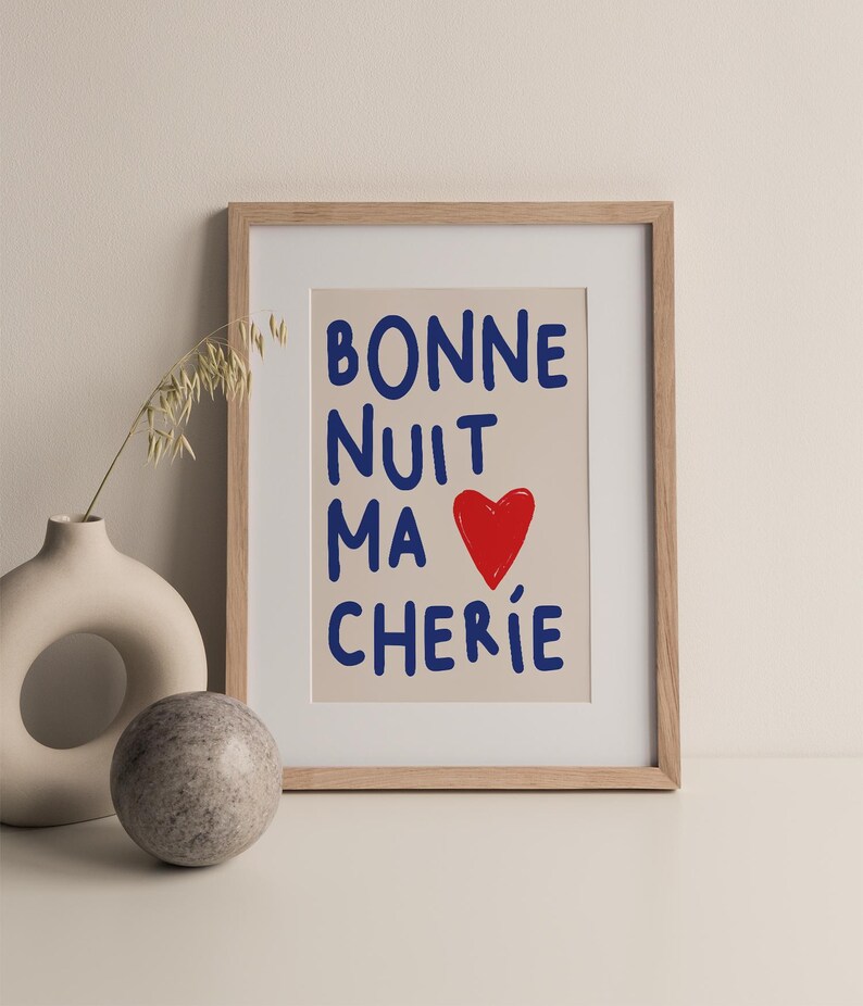 May include: A framed print with the text "BONNE NUIT MA CHERIE" in blue lettering and a red heart. The background is a light beige color.