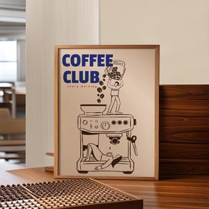 May include: A framed poster with a light beige background featuring the blue text COFFEE CLUB and the red text every morning. The illustration shows a person pouring coffee beans into a machine while another person lies underneath it.