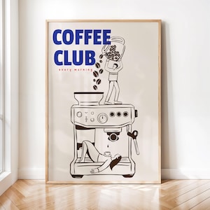 May include: A framed wall art print featuring a beige background with the blue text COFFEE CLUB and red text every morning. A line drawing shows a person pouring coffee beans into a machine while another person rests inside the machine base.