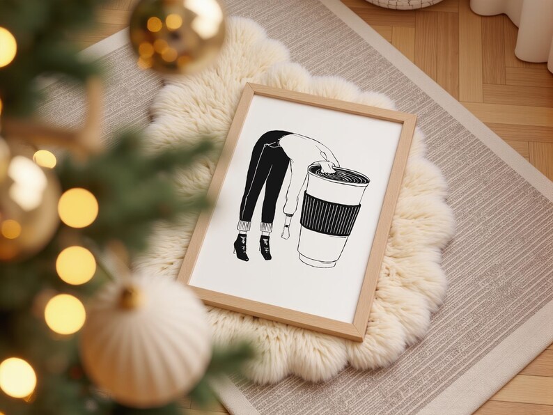 May include: A framed black and white illustration depicts a person leaning into a large coffee cup. The person's legs and torso are visible, with the head obscured. The cup has a ribbed sleeve. The artwork is set on a fluffy, white rug.