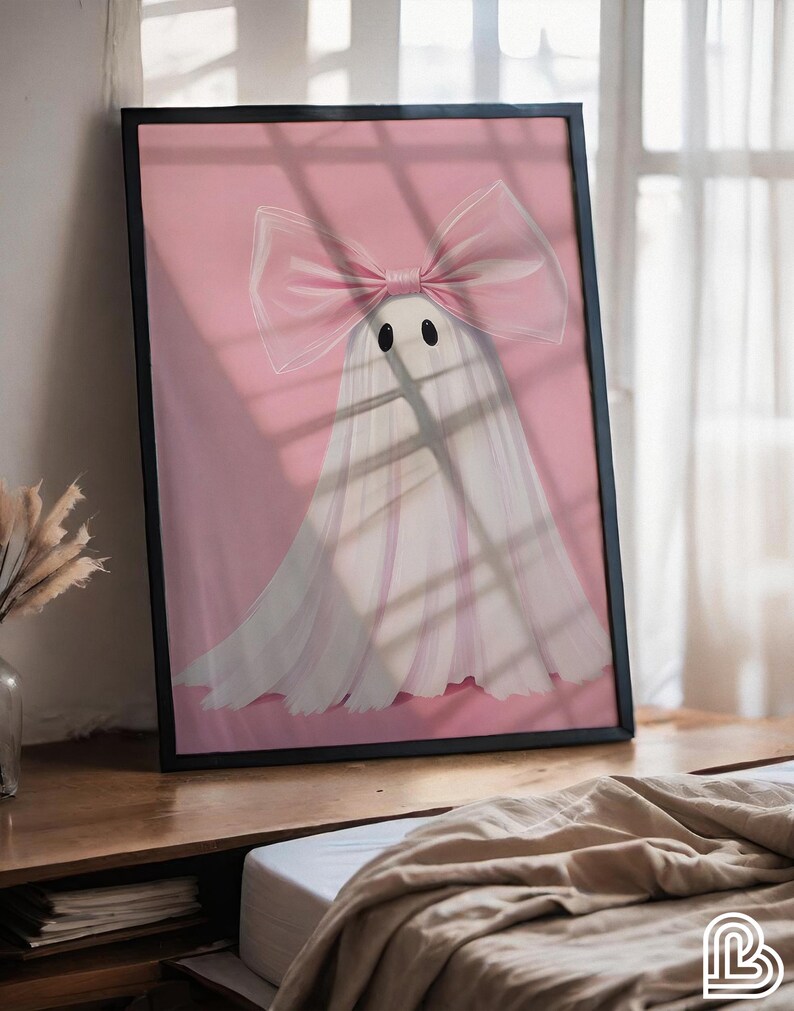 May include: Framed art print featuring a whimsical ghost design. The ghost is white with a large pink bow and black eyes, set against a pink background. The artwork is in a black frame, suitable for home decor.