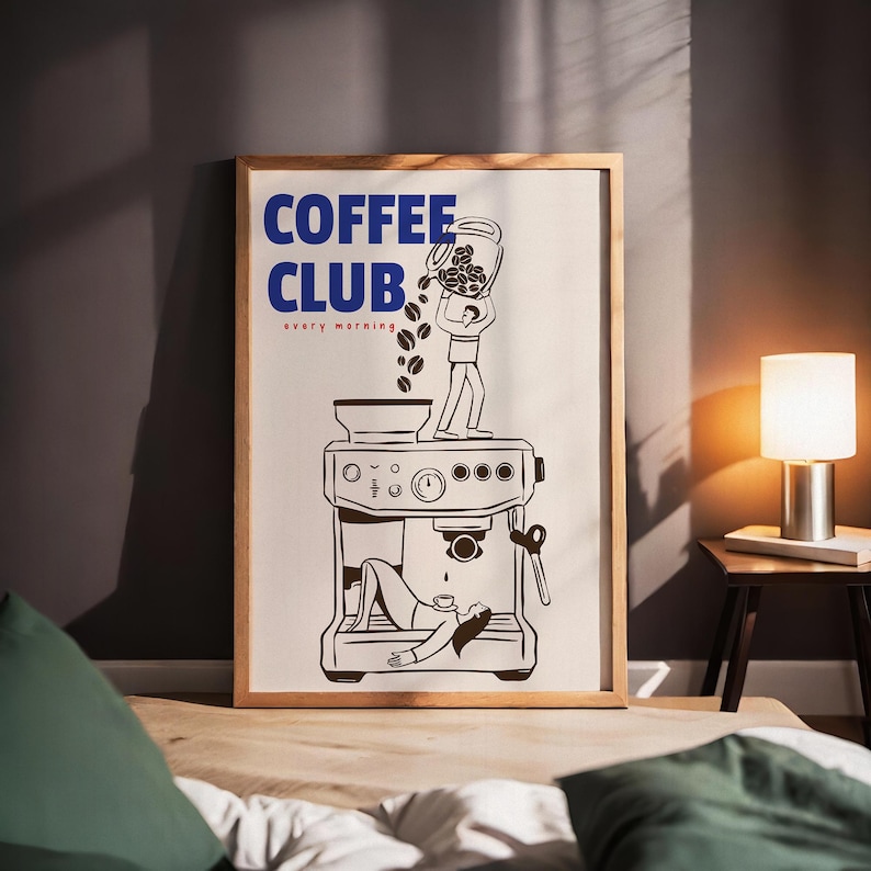 May include: A framed rectangular wall art print featuring the blue text COFFEE CLUB and red text every morning. The illustration shows a person standing on an espresso machine pouring coffee beans into it, while another person lies below.