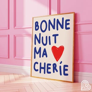 Puede incluir: Una impresión enmarcada con el texto "BONNE NUIT MA CHERIE" en letras azules y un corazón rojo. La impresión está sobre un fondo crema y está enmarcada en un marco de madera claro.