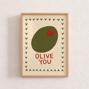 Può includere: Una stampa artistica incorniciata su sfondo color crema con una grande oliva verde scuro che presenta un piccolo cuore rosso sulla superficie. Sotto l'oliva, il testo OLIVE YOU è scritto in lettere rosse. Un bordo di piccole v verde scuro.