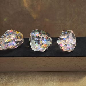 Puede incluir: Tres formas de cristal de vidrio iridiscente sobre una base de terciopelo negro dentro de una caja de madera.