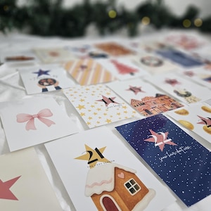 May include: A collection of Christmas-themed cards with various designs, including stars, bows, and gingerbread houses. The cards are arranged on a white surface, with some featuring text like "shine bright" and numbers.