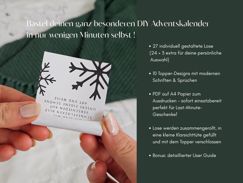 May include: A person holds a white card with black snowflake designs and text. The card is part of a DIY Advent calendar kit. The background includes a green knitted fabric and text in German.