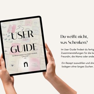 Op de afbeelding: Een tablet met een digitale gebruikershandleiding met de tekst USER GUIDE en diverse kleine grafische kaarten in roze en witte tinten. Rechts staat de Duitse tekst: Du wei&szlig;t nicht, was Schenken? Im User Guide findest du fertige Zusammenstellungen.