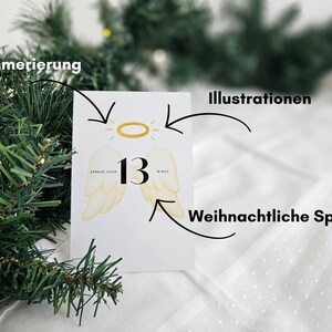 May include: A white card with the number 13, angel wings, and a golden halo illustration. The card has the text "Spread your wings". The background includes a Christmas tree branch and a white surface.