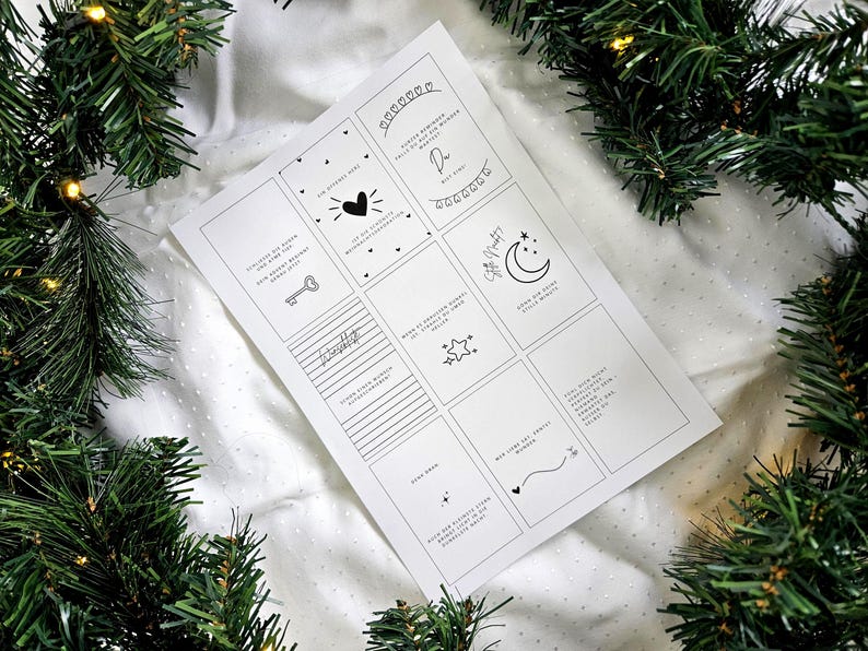 May include: A white paper sheet with multiple small, square designs, each containing a simple black illustration and text. The sheet is surrounded by green Christmas tree branches and lights.