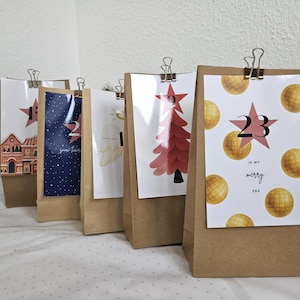 May include: Advent calendar with brown paper bags, each featuring a different festive design. The designs include a house, a starry night, an angel wing, a Christmas tree, and the number 23 with the words "in my merry era."