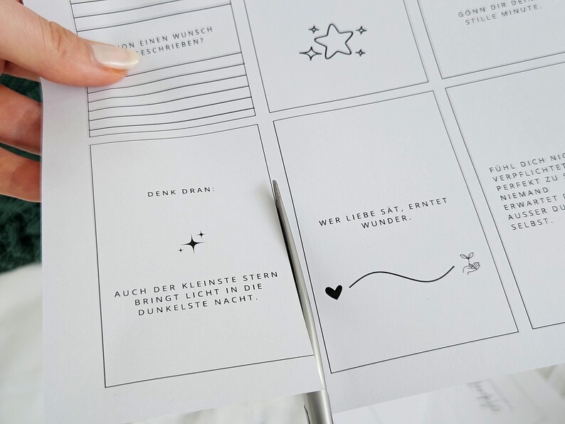 May include: A sheet of white paper with inspirational quotes and illustrations, including stars, hearts, and a sprout. The paper is being cut with scissors. The text includes phrases like "Think about it" and "Love is enough."