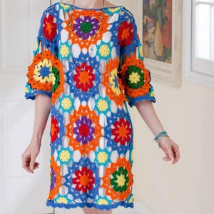Puede incluir: Vestido de ganchillo colorido con un estampado floral en tonos azules, naranjas, rojos, amarillos y verdes. El vestido tiene mangas cortas y un dobladillo a la rodilla, mostrando un diseño hecho a mano.