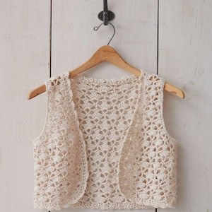 May include: A crocheted cream-coloured vest with a scalloped neckline and sleeveless design.