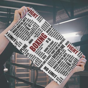 May include: A rectangular white towel with the word "BOXING" in red, surrounded by black text related to martial arts. The towel is held up by a person's hands. Keywords include Mixed Martial Arts, Fight, and Discipline.