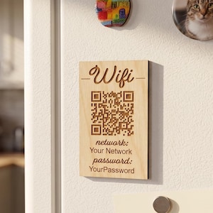 Peut inclure: Une plaque rectangulaire en bois clair avec un code QR gravé au laser et le texte Wifi, network: Your Network, et password: YourPassword. La plaque est fixée sur une surface blanche avec d'autres aimants et une liste de courses.